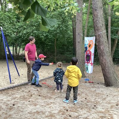 Bild vergr&ouml;&szlig;ern: Ein Kind wirft bei einem Wurfspiel auf dem Spielplatz ein S&auml;ckchen, zwei Kinder und ein Erwachsener schauen dabei zu.