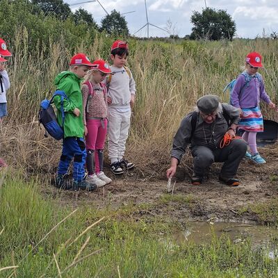 Bild vergr&ouml;&szlig;ern: Der J&auml;ger zeigt den Kindern Spuren an einem Wasserloch.