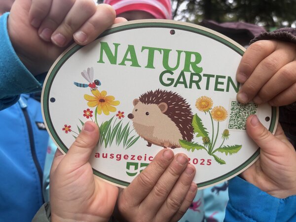 So sieht unsere Naturgarten-Plakette aus. Kinder halten sie in ihren H&auml;nden. 