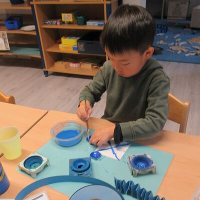 Bild vergr&ouml;&szlig;ern: Den Kindern stehen diverse blaue Utensilien zur Verwendung. Ein Junge entscheidet sich f&uuml;r Wasser- und Fingerfarben und gestaltet damit sein Bild.