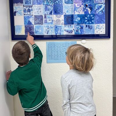 Bild vergr&ouml;&szlig;ern: Zwei Jungs schauen sich das Kunstwerk an und zeigen sich ihre Bilder. Sie erkennen auch andere Namen auf der Legende und ordnen anhand der Legende die Bilder zu.