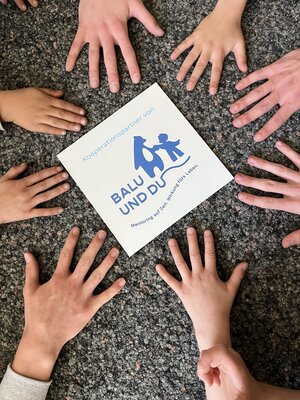 Bild vergr&ouml;&szlig;ern: acht H&auml;nde umschlie&szlig;en das Logo "Balu und du" am 28.04.2026