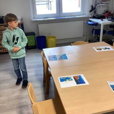 Bild vergr&ouml;&szlig;ern: Auf einem Tisch liegen f&uuml;nf Bilder f&uuml;r die Namensvorschl&auml;ge. Ein Kind l&auml;uft um den Tisch herum und sucht f&uuml;r seinen Wunschnamen das passende Foto.