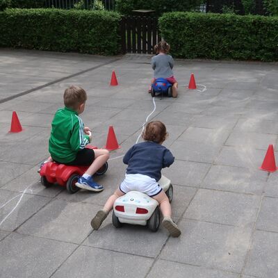 Bild vergr&ouml;&szlig;ern: Drei Kinder fahren mit einem blauem, rotem bzw. wei&szlig;em Bobbycar im Slalom nebeneinander.