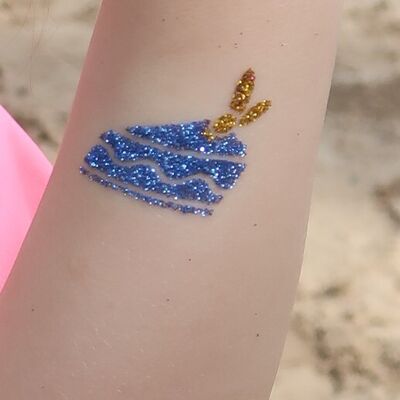 Bild vergr&ouml;&szlig;ern: Glitzertattoo auf einem Unterarm - eine blaue Glitzertorte aus der ein goldener Hase hervorschaut.