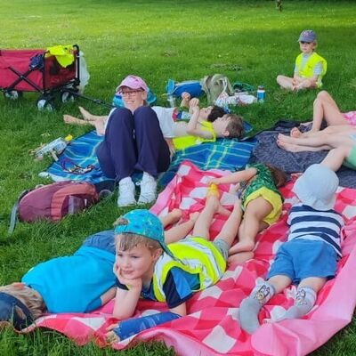 Kinder mit Sonnenh&uuml;ten liegen oder sitzen mit ihrer p&auml;dagogischen Fachkraft auf blau- und rotkarierten Picknickdecken.